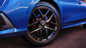Close up of the front wheel on a parked blue Civic Sedan in a dark warehouse-like space.