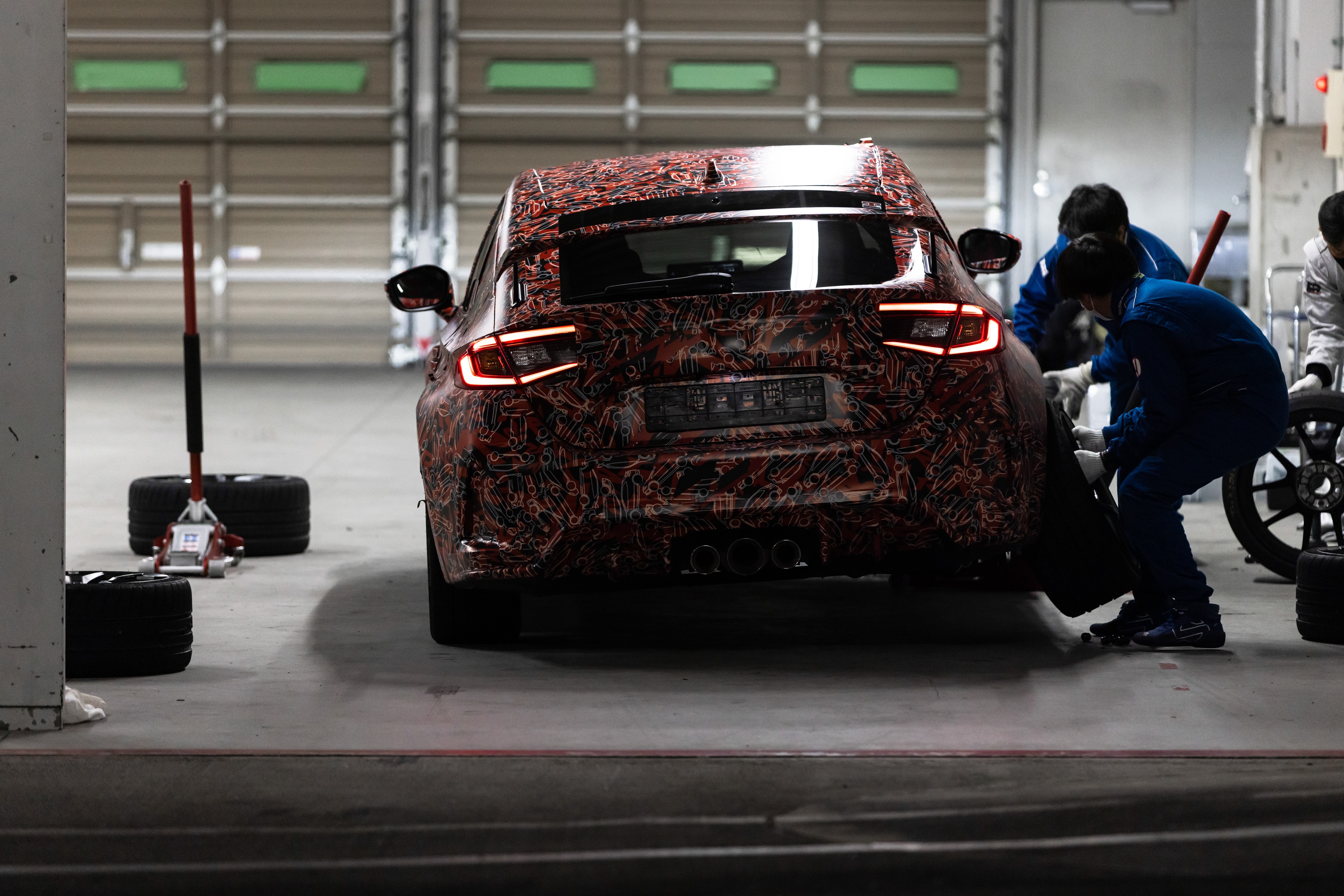 Rear view of the 2023 Honda Civic Type R prototype parked in a garage, undergoing a wheel change