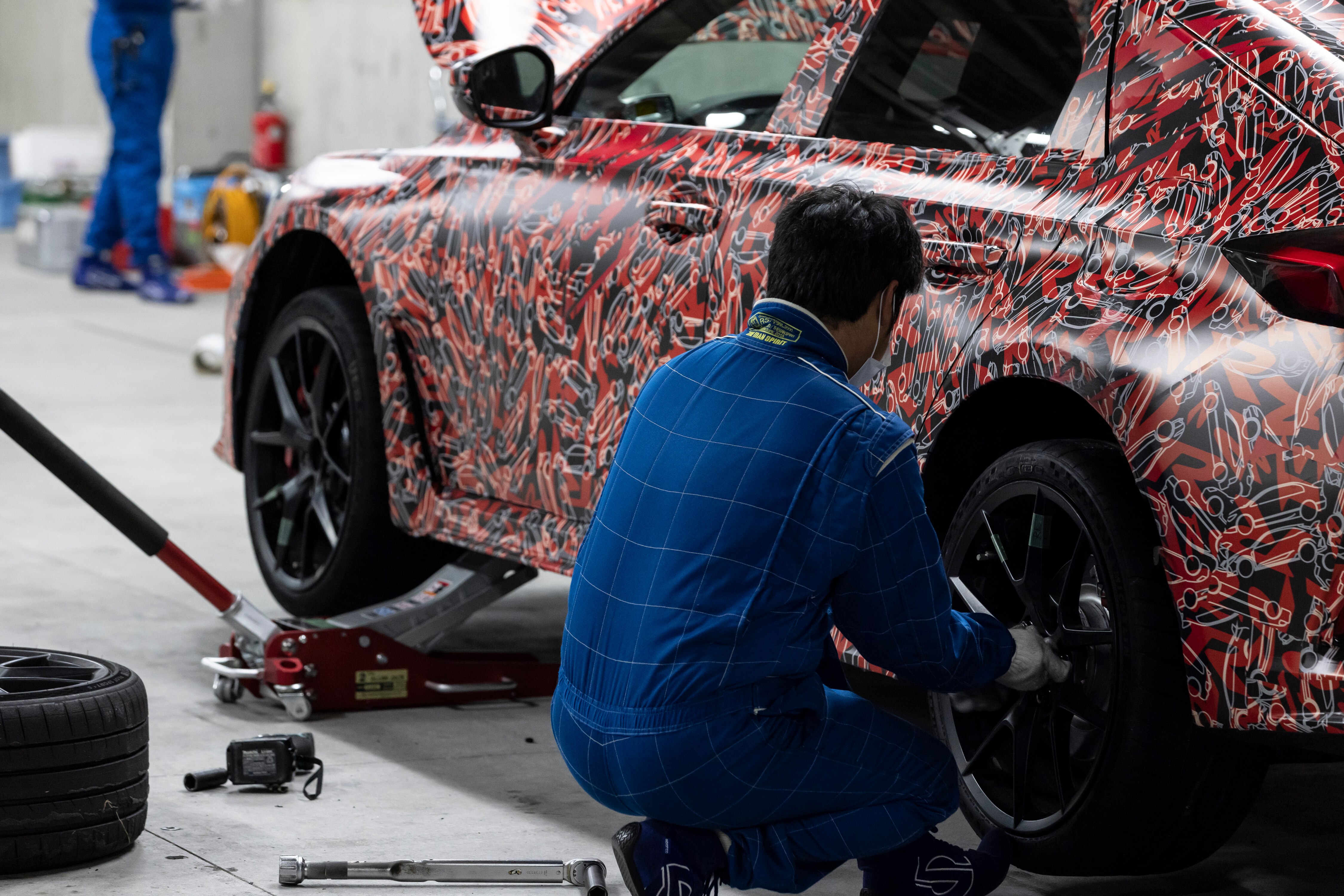 Driver-side view of the 2023 Honda Civic Type R prototype in a garage, with a testing engineer working on the rear driver-side wheel.