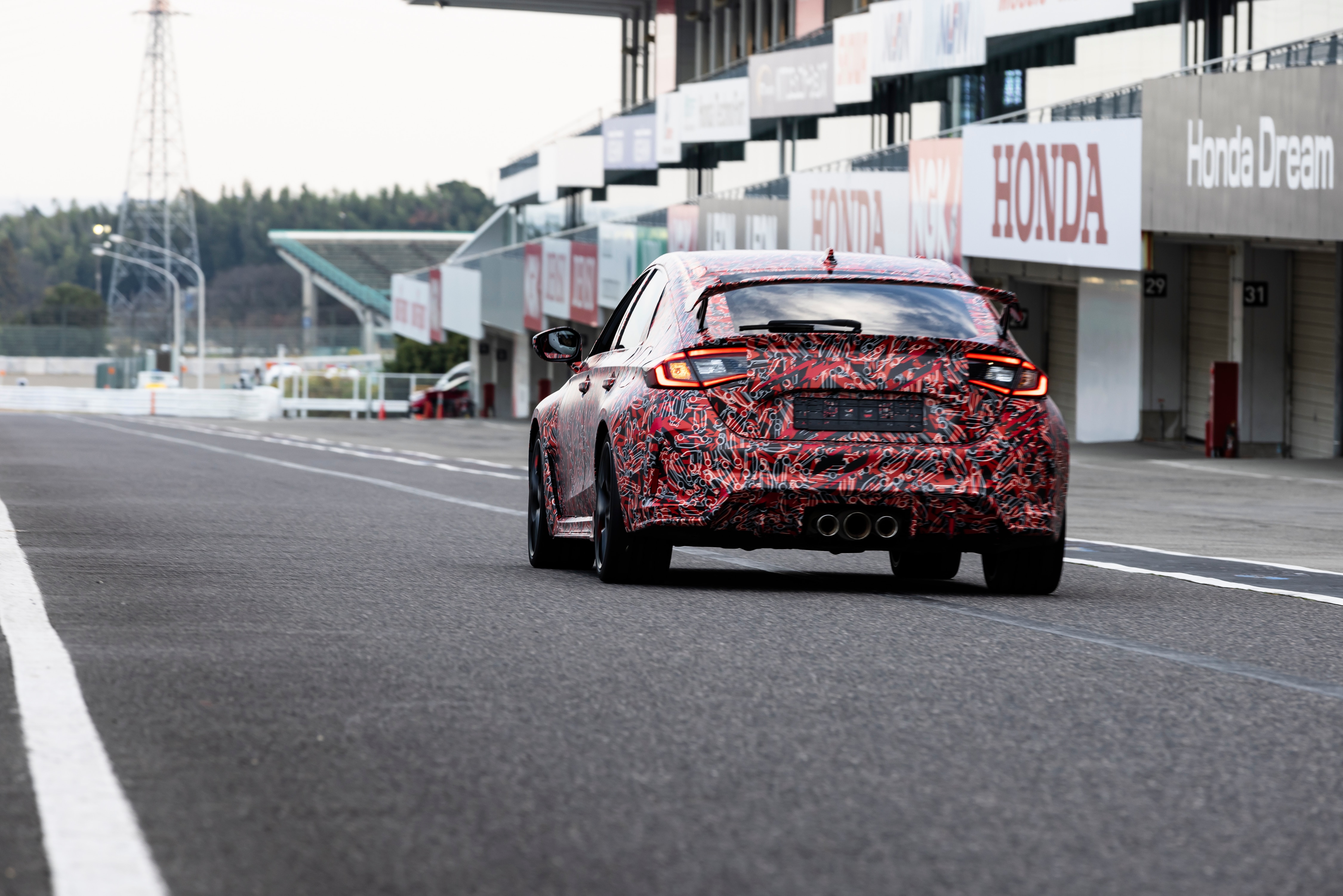 Rear driver-side view of the 2023 Honda Civic Type R prototype driving on the Suzuka Circuit racetrack.
