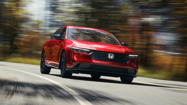 Plan de trois quarts avant d’une Accord rouge qui roule vers la caméra dans un virage sur l’autoroute, dans une forêt tempérée, de jour.