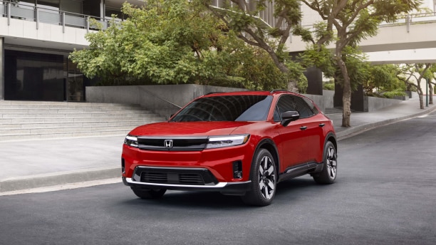 Side view of red Prologue plugged into a charger in a modern house’s carport.