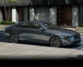 3/4 side view of grey Accord parked curbside on a sunny day in an upscale urban neighbourhood, with wooden townhome garage doors behind it.