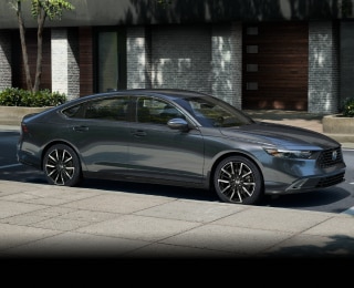 3/4 side view of grey Accord parked curbside on a sunny day in an upscale urban neighbourhood, with wooden townhome garage doors behind it.
