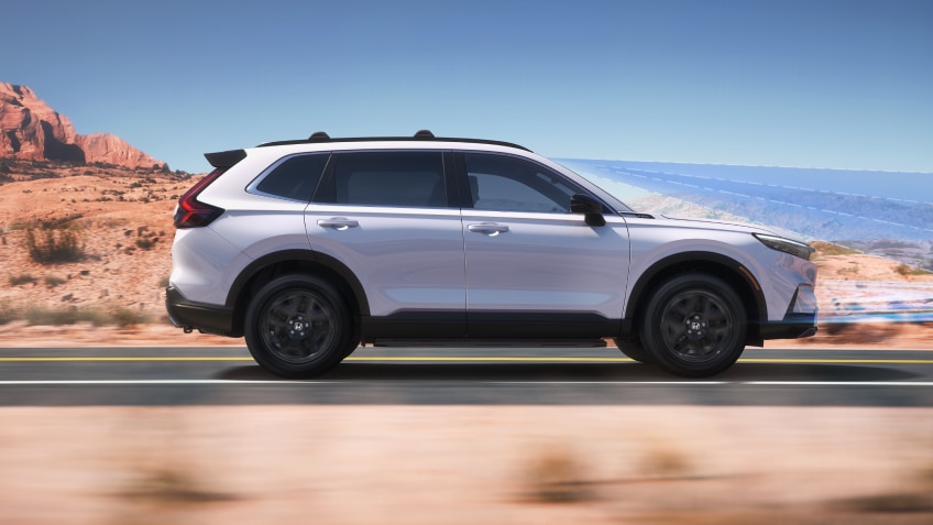 Vue latérale d’un CR-V blanc roulant sur une autoroute dans le désert.