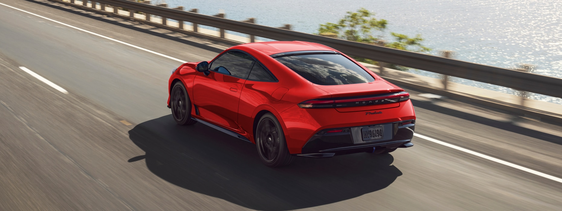 Vue arrière d'une Prelude rouge roulant sur une route côtière.