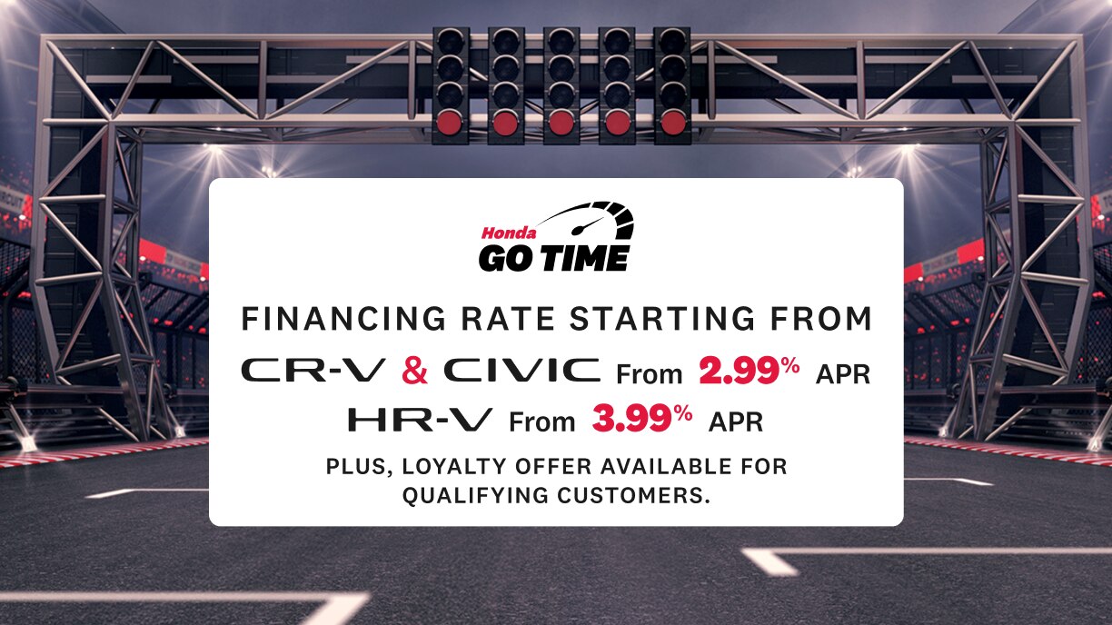 A racetrack inside a stadium with overhead lights and a starting gantry displaying a Honda “Go Time” sign. The sign lists financing rates for CR-V (2.99% APR), Civic (2.99% APR), and HR-V (3.99% APR). Text in the lower left reads “Get on track to your next Honda”, sub-copy reads “Conditions apply. Click Learn more for details” with a “Learn More” button below.