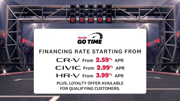 A racetrack inside a stadium with overhead lights and a starting gantry displaying a Honda “Go Time” sign. The sign lists financing rates for CR-V (2.99% APR), Civic (2.99% APR), and HR-V (3.99% APR). Text in the lower left reads “Get on track to your next Honda”, sub-copy reads “Conditions apply. Click Learn more for details” with a “Learn More” button below.