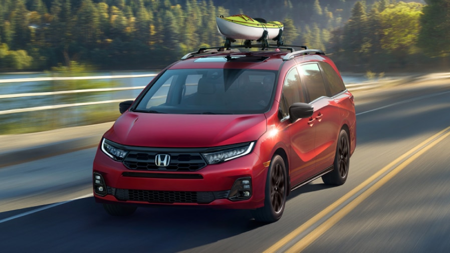 3/4 front view of red Odyssey driving on lakeside road.