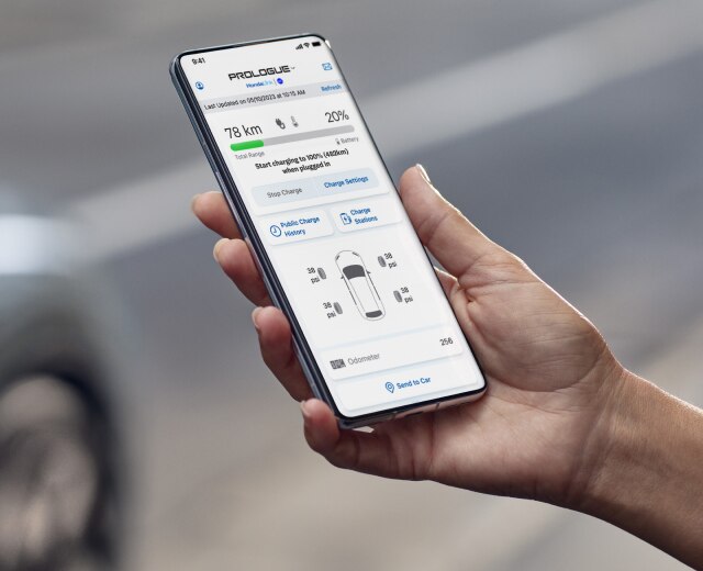 Une main tient un appareil sur lequel l’application HondaLink est ouverte, avec un véhicule Honda en arrière-plan. 