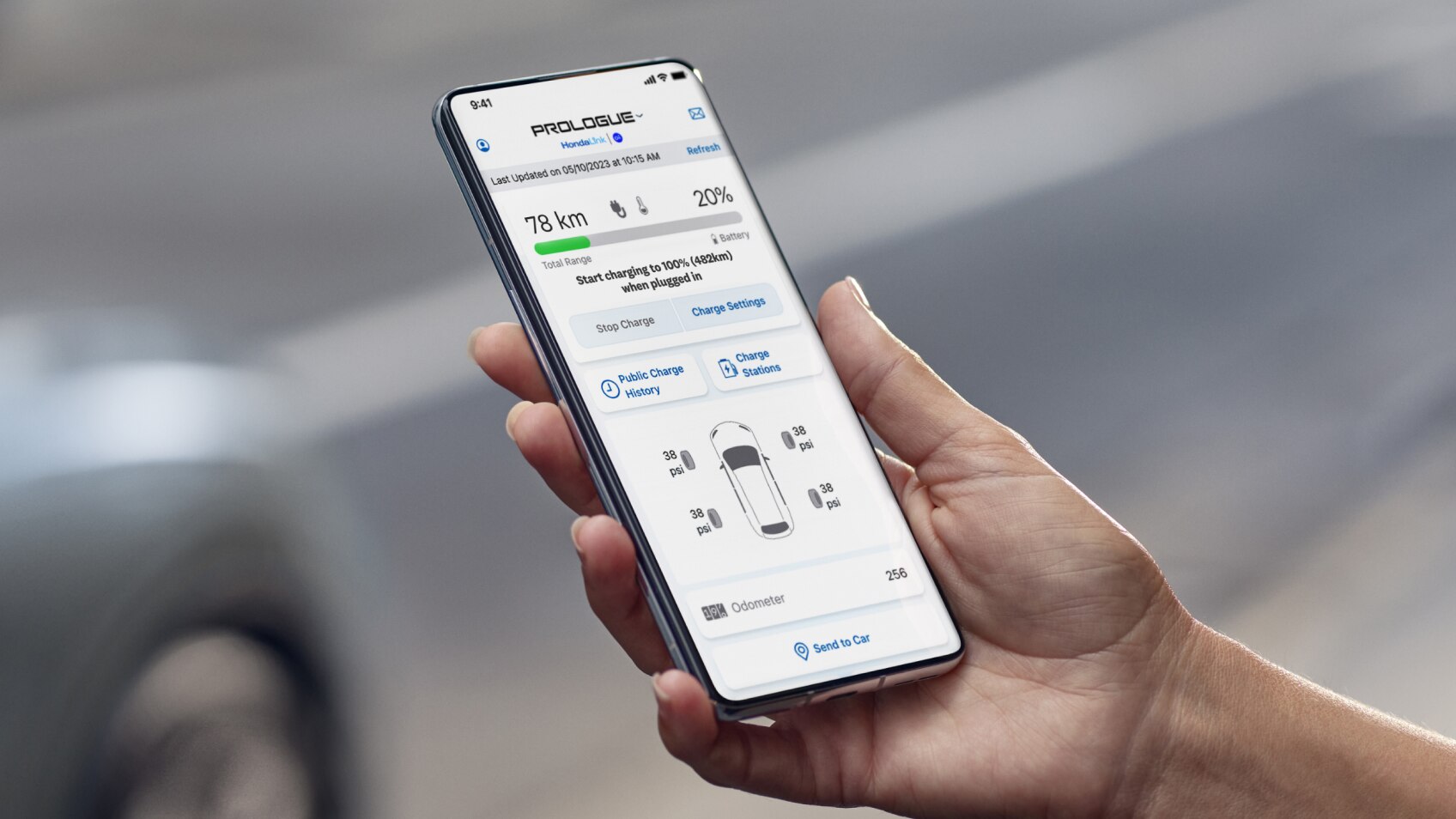 Une main tient un appareil sur lequel l’application HondaLink est ouverte, avec un véhicule Honda en arrière-plan. 