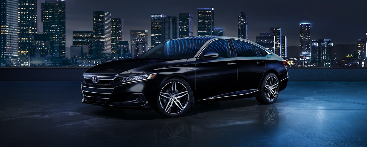 "3/4 front sideview of black Accord Hybrid on rooftop at night. City skyline behind it.  "