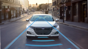 Front view of white Accord Hybrid driving on city street. Blue sensor waves and lines emit from the front.