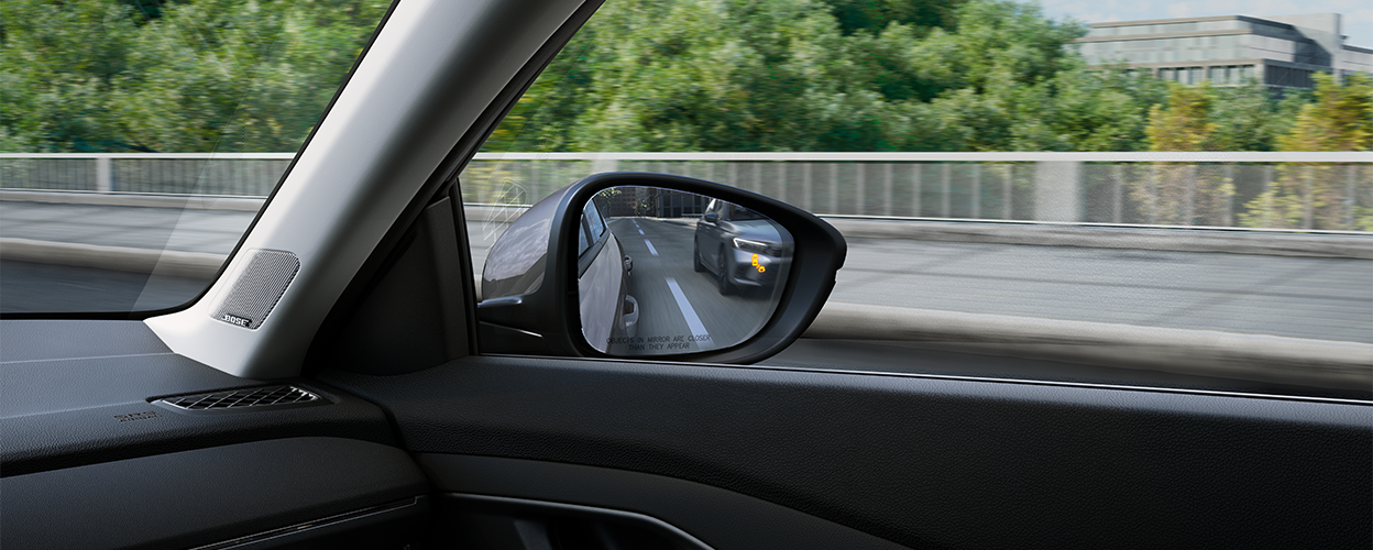 Interior view of door mirror with the Blind Spot Indicator light on, reflecting a car in the other lane.
