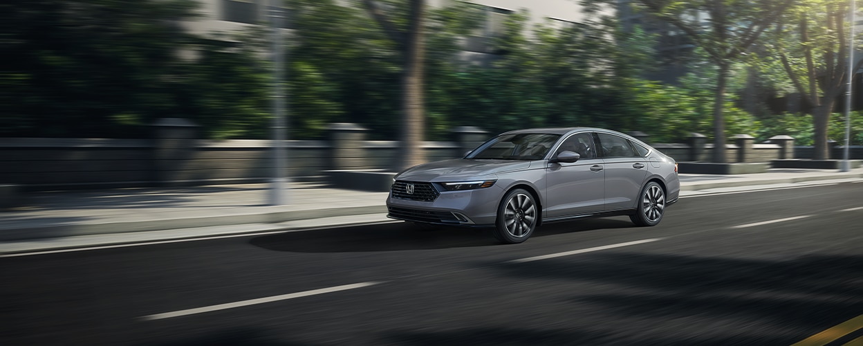 3/4 front view of grey Accord driving on upper-class city street lined with trees. 