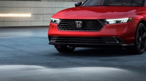 Plan moyen 3/4 avant d’une Accord rouge stationnée devant un immeuble en bloc de béton.