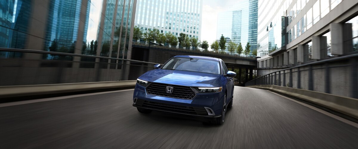 Plan avant d’une Accord bleue roulant vers la caméra dans une rue urbaine vide au milieu de bâtiments.