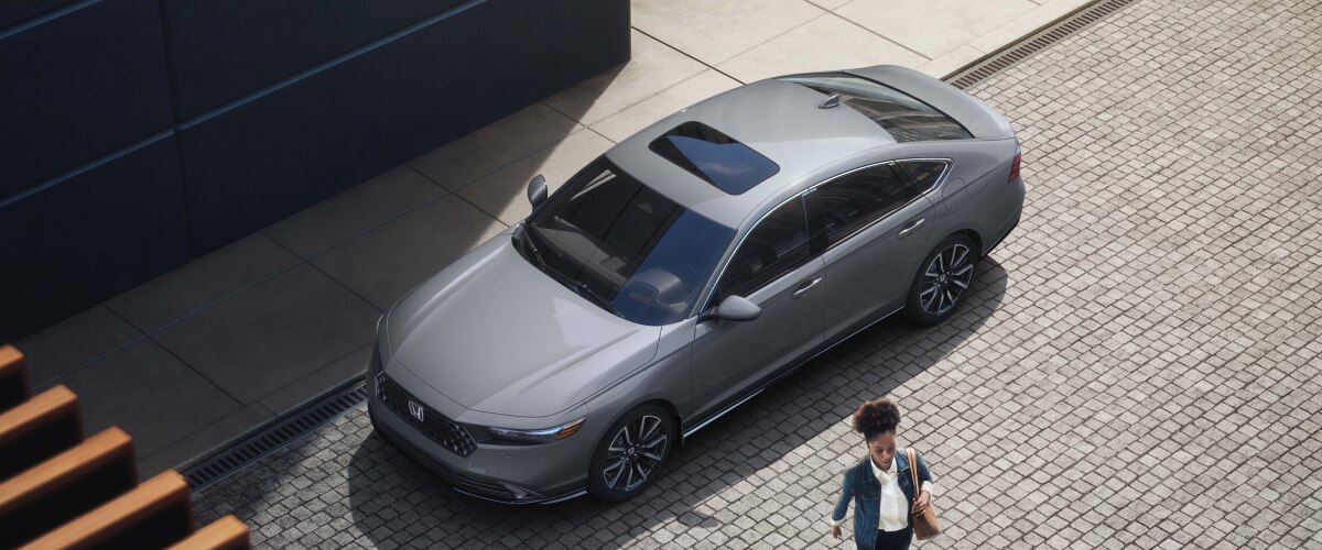 Plan de trois quarts en plongée d’une femme s’éloignant d’une Accord grise stationnée en bordure de rue dans un chic quartier urbain.