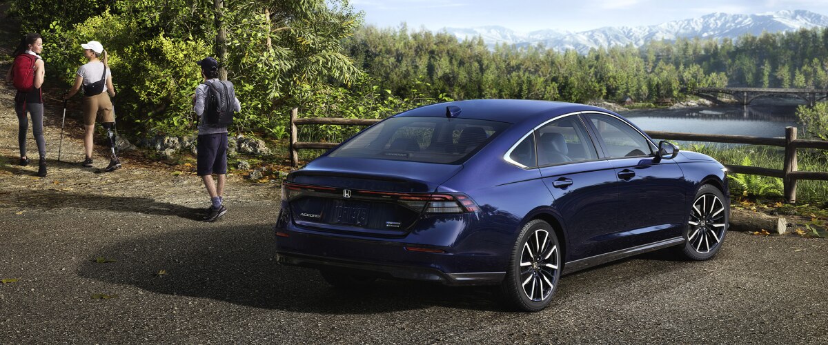Plan de trois quarts arrière d’une Accord bleue stationnée avec vue sur une forêt et des montagnes. Un randonneur s’en éloigne.