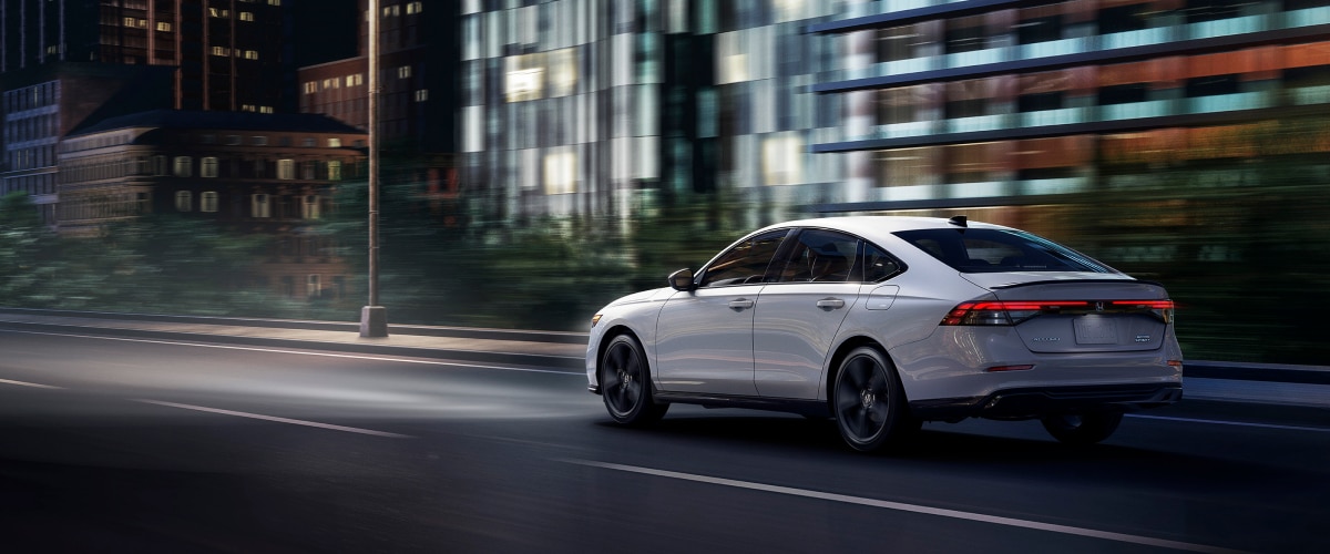 Plan de trois quarts arrière d’une Accord blanche circulant de nuit sur une autoroute devant des bâtiments.