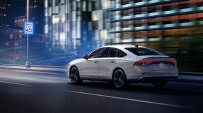 Plan de trois quarts arrière d’une Accord blanche circulant de nuit sur une autoroute devant des bâtiments. Des lignes de capteur bleues sont émises de l’avant et détectent un panneau routier.