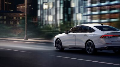 Plan de trois quarts arrière d’une Accord blanche circulant de nuit sur une autoroute devant des bâtiments.
