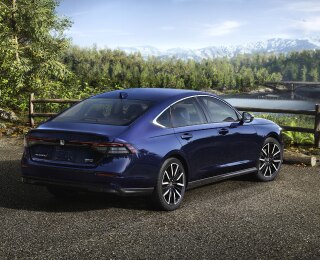 Plan de trois quarts arrière d’une Accord bleue stationnée avec vue sur une forêt et des montagnes. Un randonneur s’en éloigne.