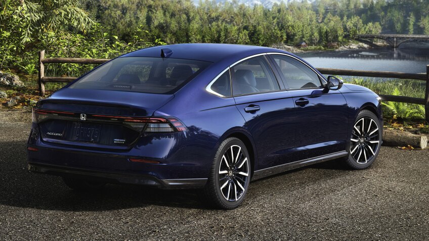 Plan de trois quarts arrière d’une Accord bleue stationnée avec vue sur une forêt et des montagnes. Un randonneur s’en éloigne.