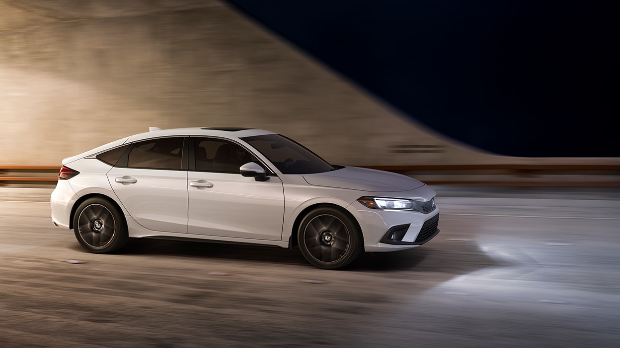 3/4 side front view of white Hatchback exiting a tunnel at night.