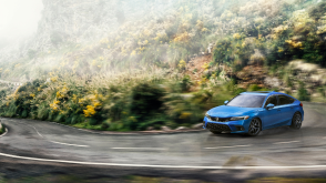 3/4 front view of blue Hatchback taking a turn on a a tropical forest highway. 
