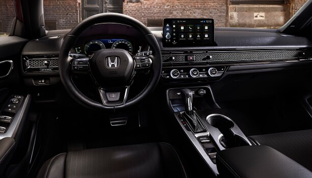 Vue panoramique intérieure du pare-brise d’une Civic à hayon stationnée devant le mur de briques d’un vieil entrepôt.