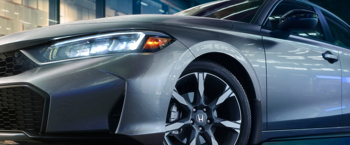 Gros plan de l’avant d’une Civic à hayon grise avec les phares allumés. 