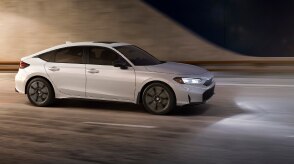 Plan de trois quarts de l’avant d’une Civic à hayon blanche sortant d’un tunnel la nuit.