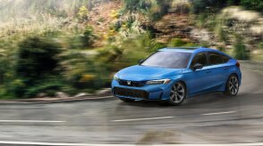 Plan de trois quarts avant d’une Civic à hayon bleue dans un virage sur une route forestière tropicale.