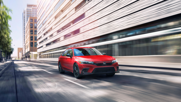 3/4 front view of red Civic Sedan driving in the city at during the day.