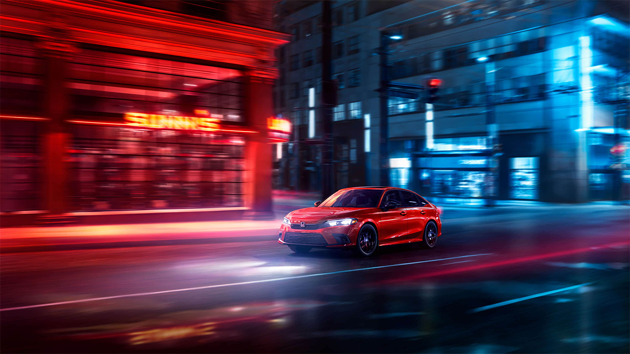 3/4 front view of red Honda Civic Sedan driving in the city at night.