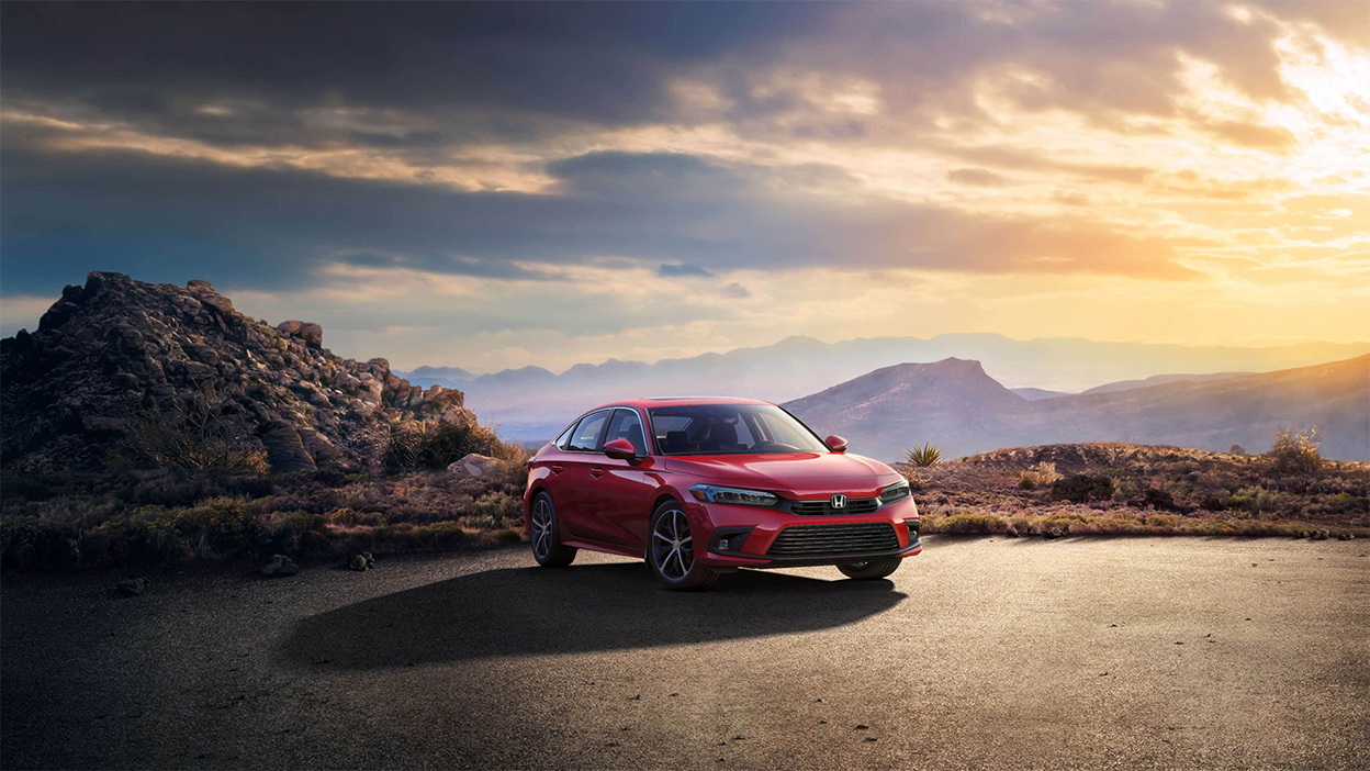 3/4 view of a parked red Honda Civic Sedan at sunset with desert hills in the background.