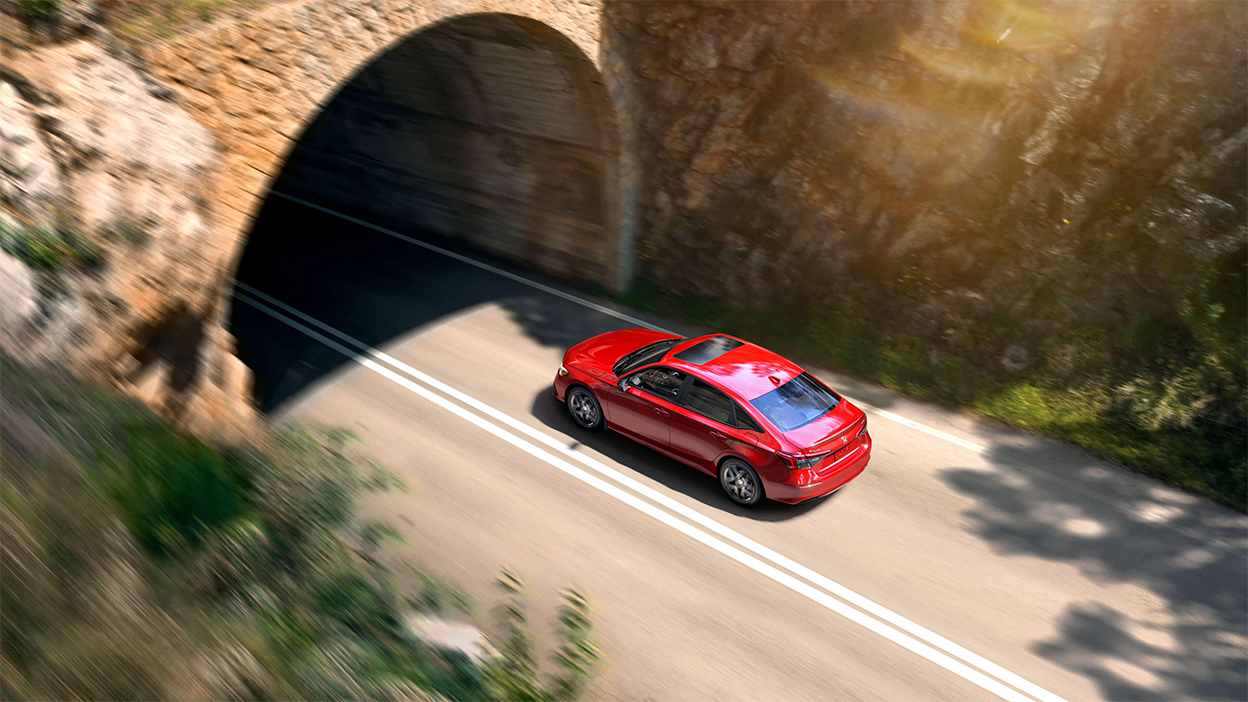 3/4 rear bird’s eye view of red Honda Civic Sedan driving into a mountainside tunnel.