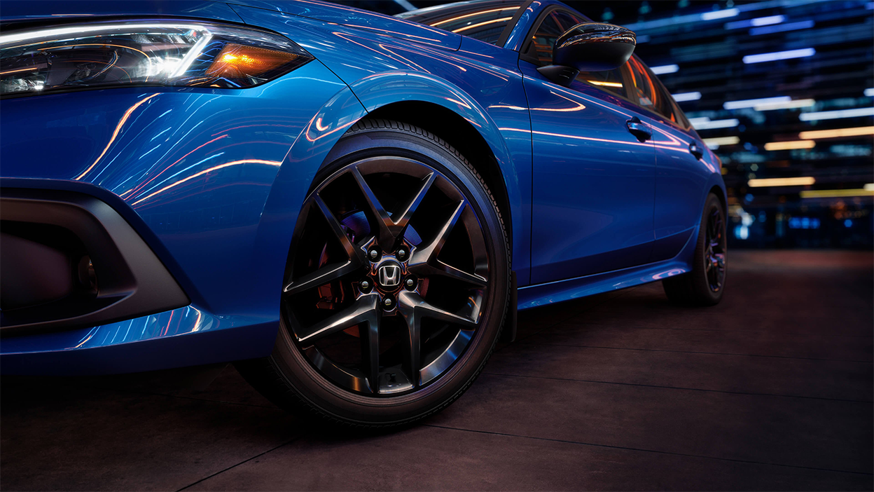 Closeup of the front wheel on a parked blue Honda Civic Sedan in a dark warehouse-like space.