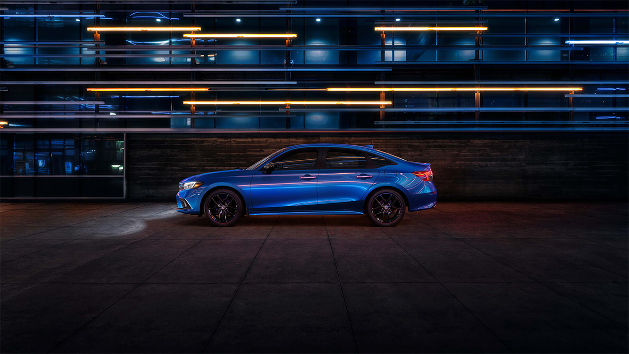 Side view of a parked blue Honda Civic Sedan in a dark warehouse-like space.