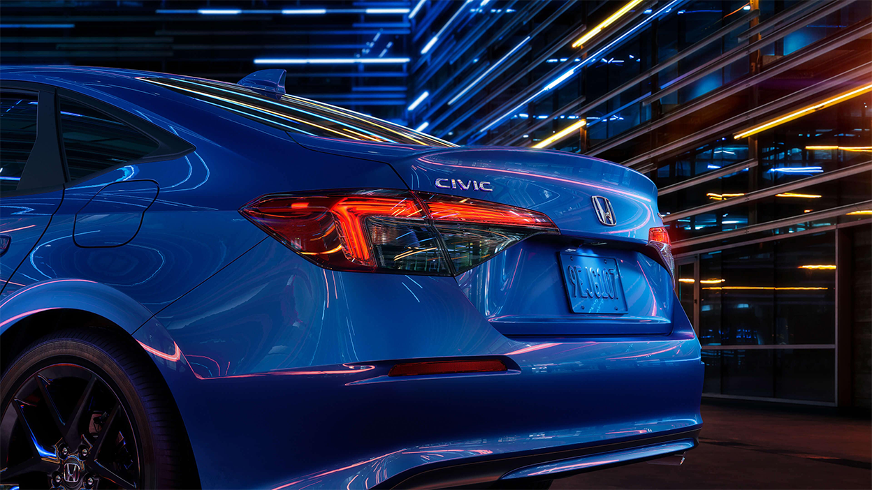 3/4 view close up of taillight and trunk of a blue Civic Sedan in a dark warehouse-like space.