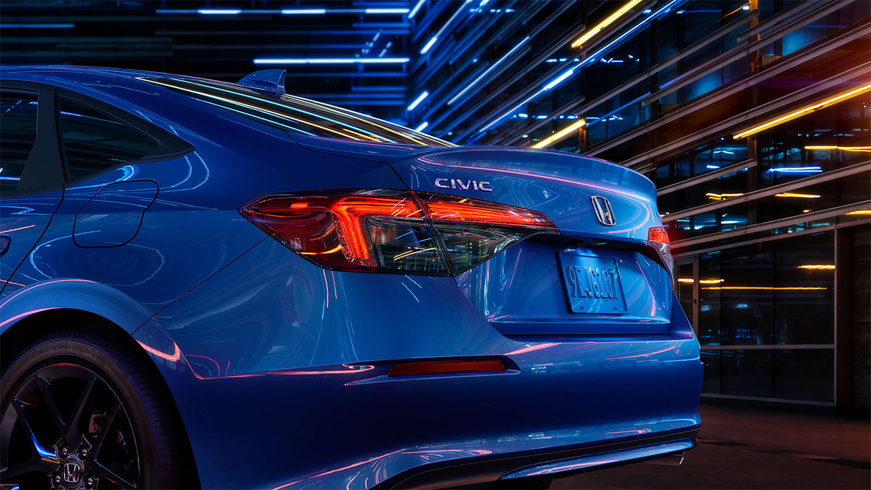 3/4 view close up of taillight and trunk of a blue Honda Civic Sedan in a dark warehouse-like space.