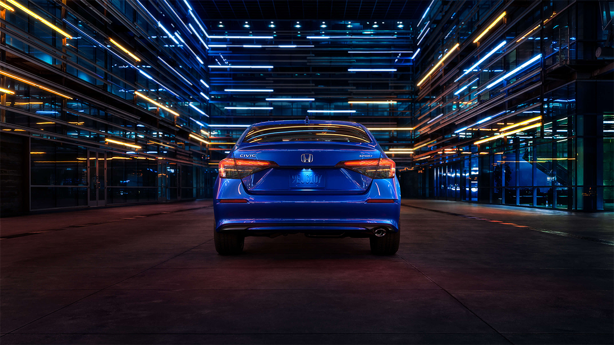 Rear view of a parked blue Civic Sedan in a dark warehouse-like space.