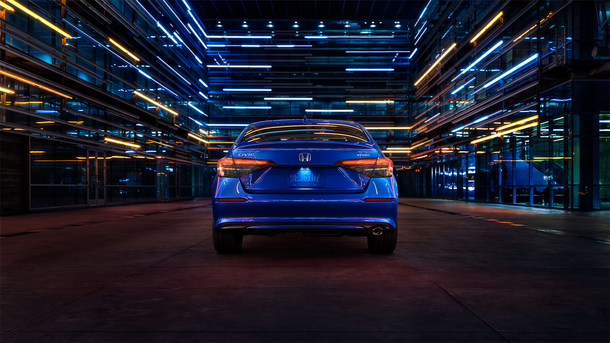 Rear view of a parked blue Honda Civic Sedan in a dark warehouse-like space.