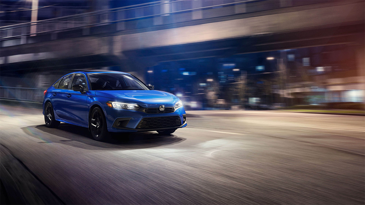 3/4 front view of blue Honda Civic Sedan driving off a city offramp at night.