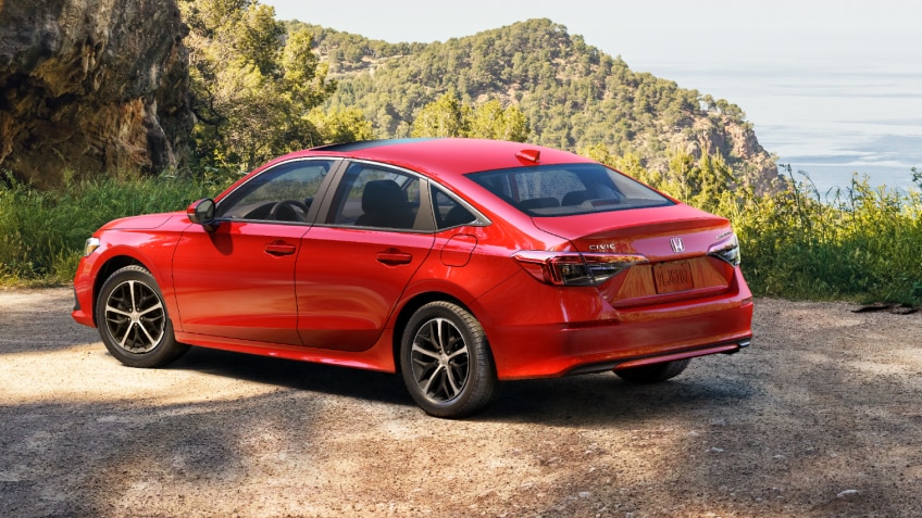3/4 side rear view of red Civic Sedan parked at a scenic lookout spot overlooking plush green hills.