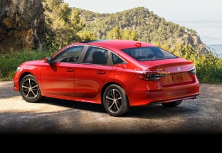 3/4 side rear view of red Civic Sedan parked at a scenic lookout spot overlooking plush green hills.