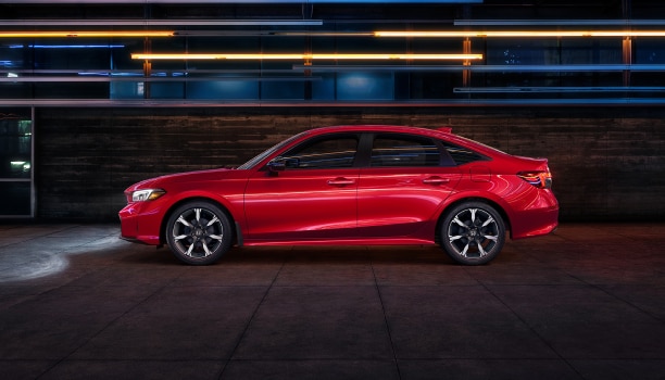 Side wide view of a parked red Civic Sedan in a dark warehouse-like space.