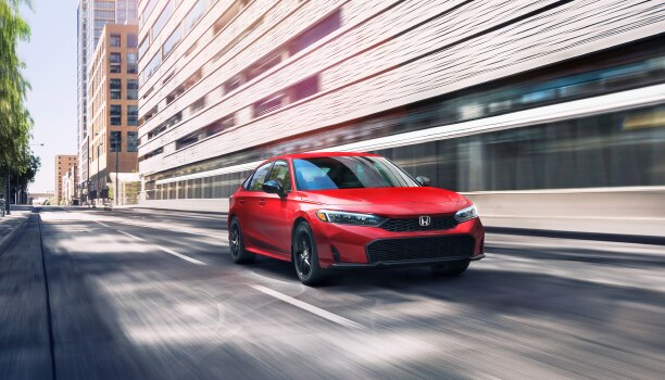 3/4 front view of red Civic Sedan driving in the city at during the day.
