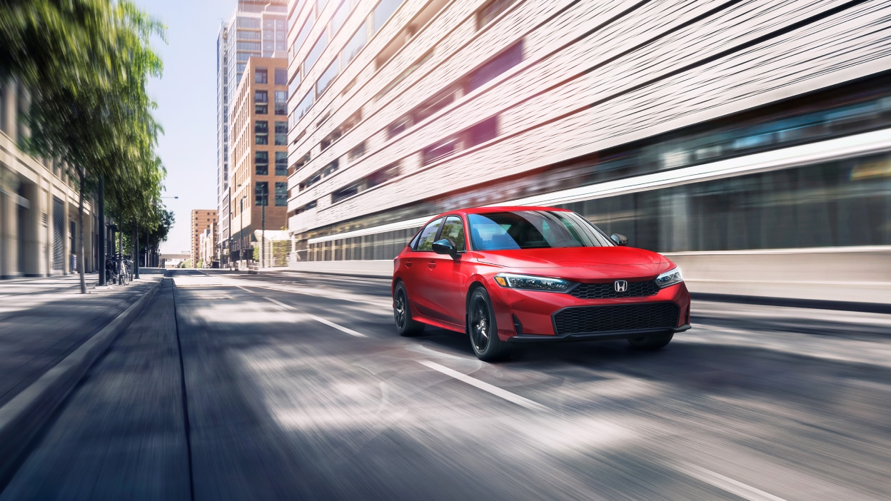 3/4 front view of red Civic Sedan driving in the city at during the day.